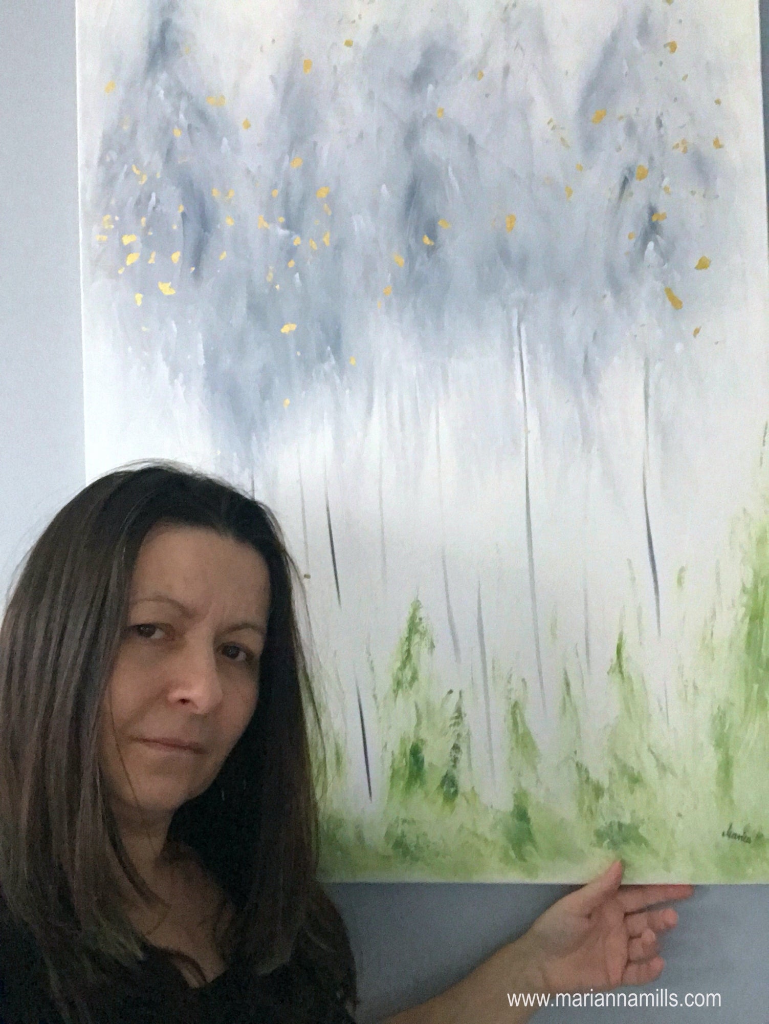 original surreal oil painting with 22k gold leaves by Marianna Mills, Hungarian artist. title is The first of Phoenix and it featuring gray trees with white background and fresh green grass. Marianna the artist took a selfie in front of her painting.